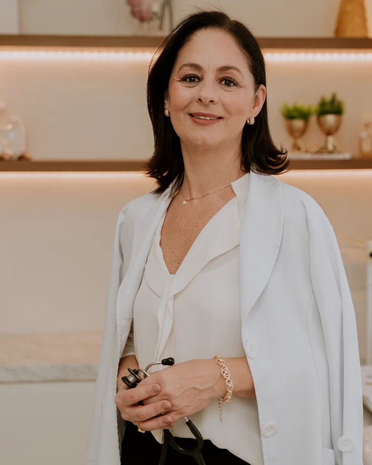 Dra. Vanessa Pozzo de jaleco, segurando o estetoscópio, no consultório
